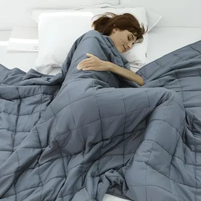 Quilted gray weighted blanket folded neatly at the foot of an inviting bed layered with neutral pillows and soft throws