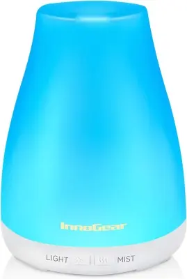 Ceramic ultrasonic essential oil diffuser releasing gentle aromatic cool mist on a tidy bedside table next to fresh eucalyptus