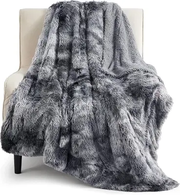 Super soft ivory faux fur throw blanket casually draped across a plush duvet in a warm sunlit Scandinavian bedroom