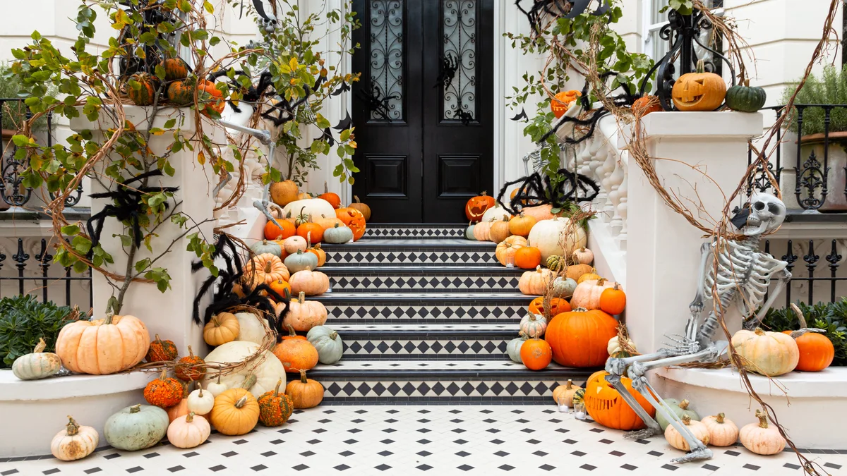 Grand front porch staircase cascading with white, gray, and muted heirloom pumpkins accented by black spiders and creeping vines
