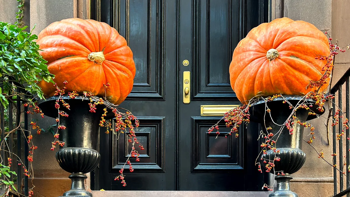 Flanking black cast iron urns holding oversized fairytale pumpkins and trailing dried red berry branches by front door