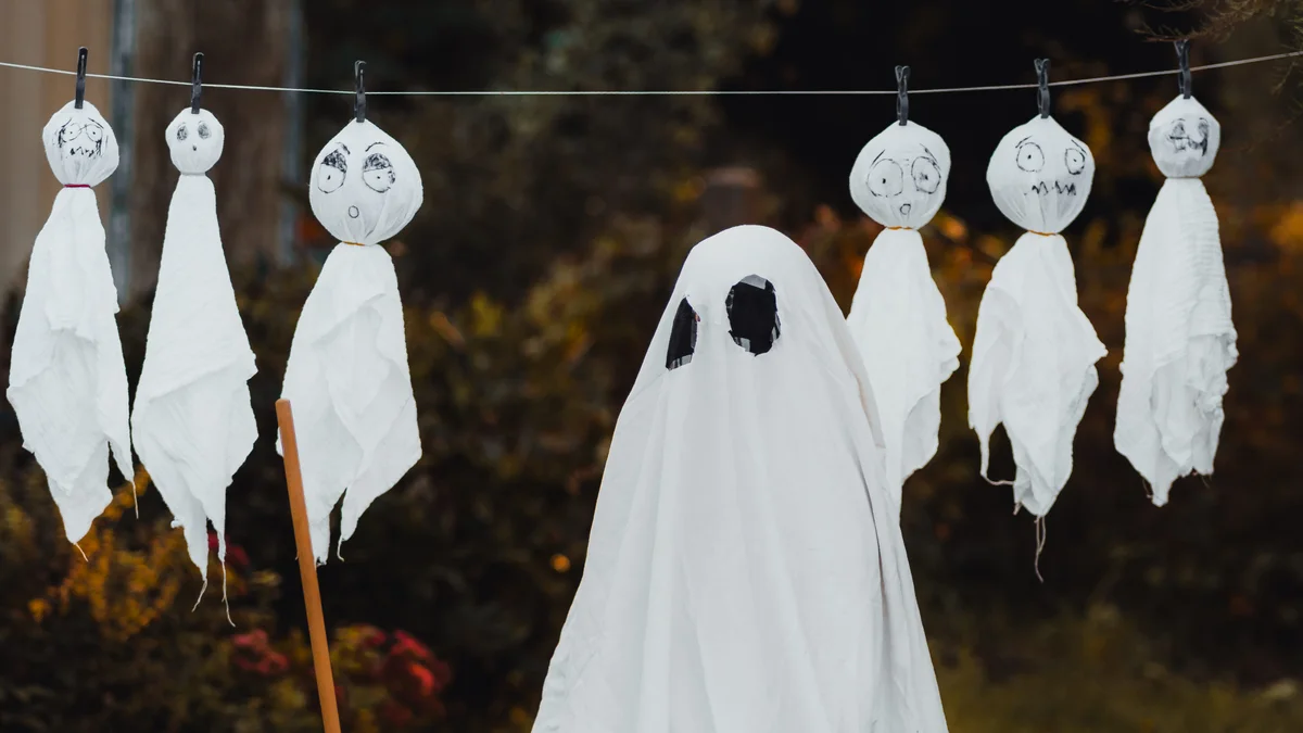 Tasteful garden display featuring outdoor ghosts draped in flowing white fabric with vintage watering cans and rustic broom