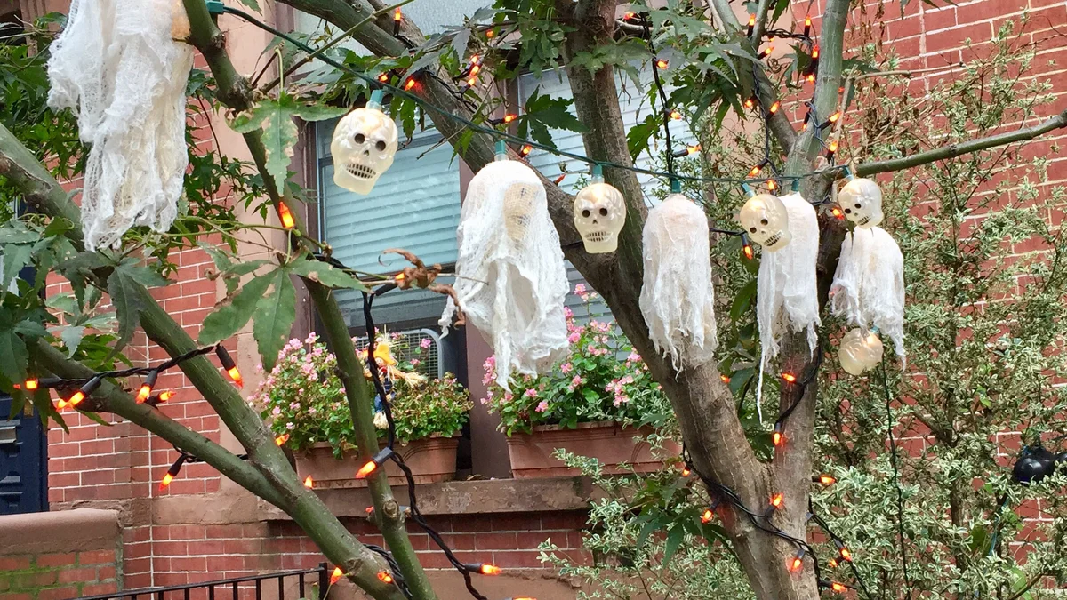 Verdant garden tree decorated with illuminated skull string lights and hanging cheesecloth phantoms nestled in lush foliage