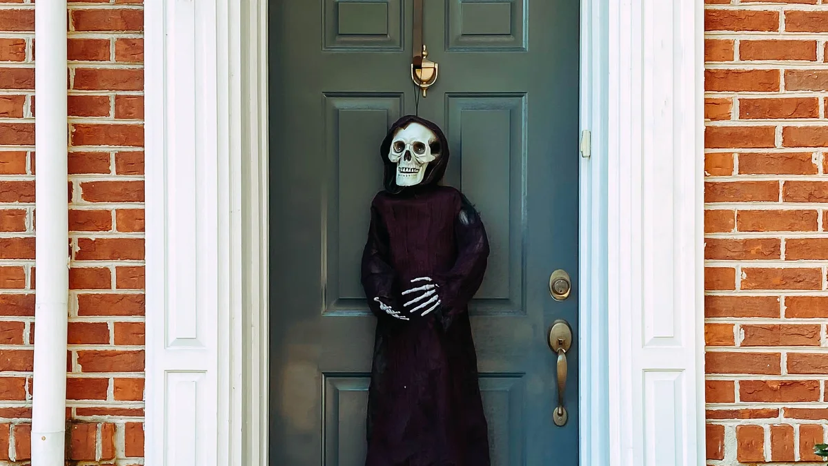 Classic painted front door adorned with a sleek hanging grim reaper figure and crisp symmetrical red mums