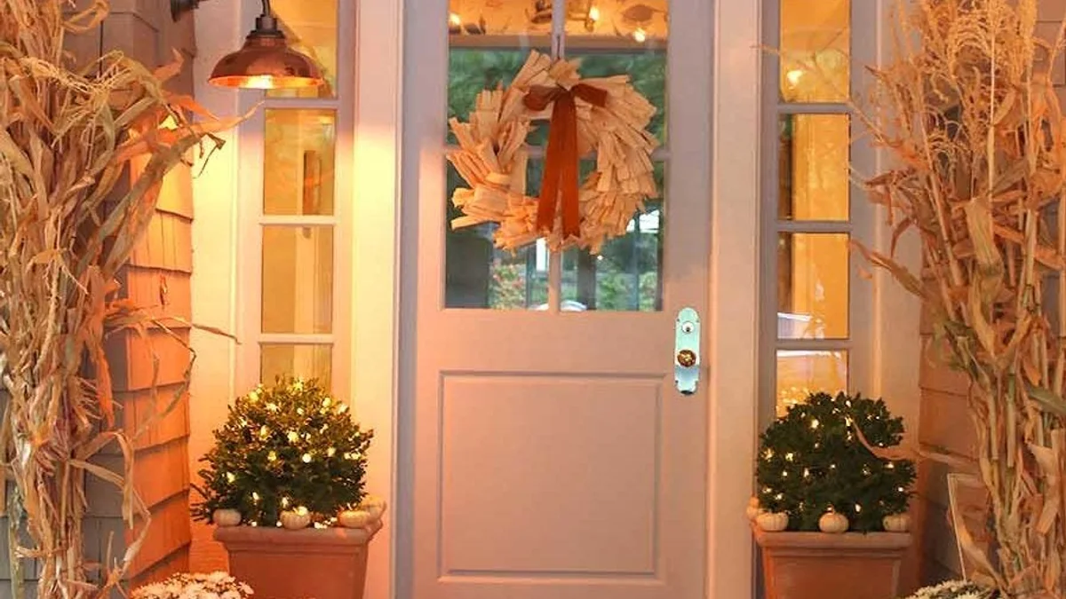Traditional farmhouse front porch with tall dried corn stalk bundles tied to porch posts with wide black satin ribbons
