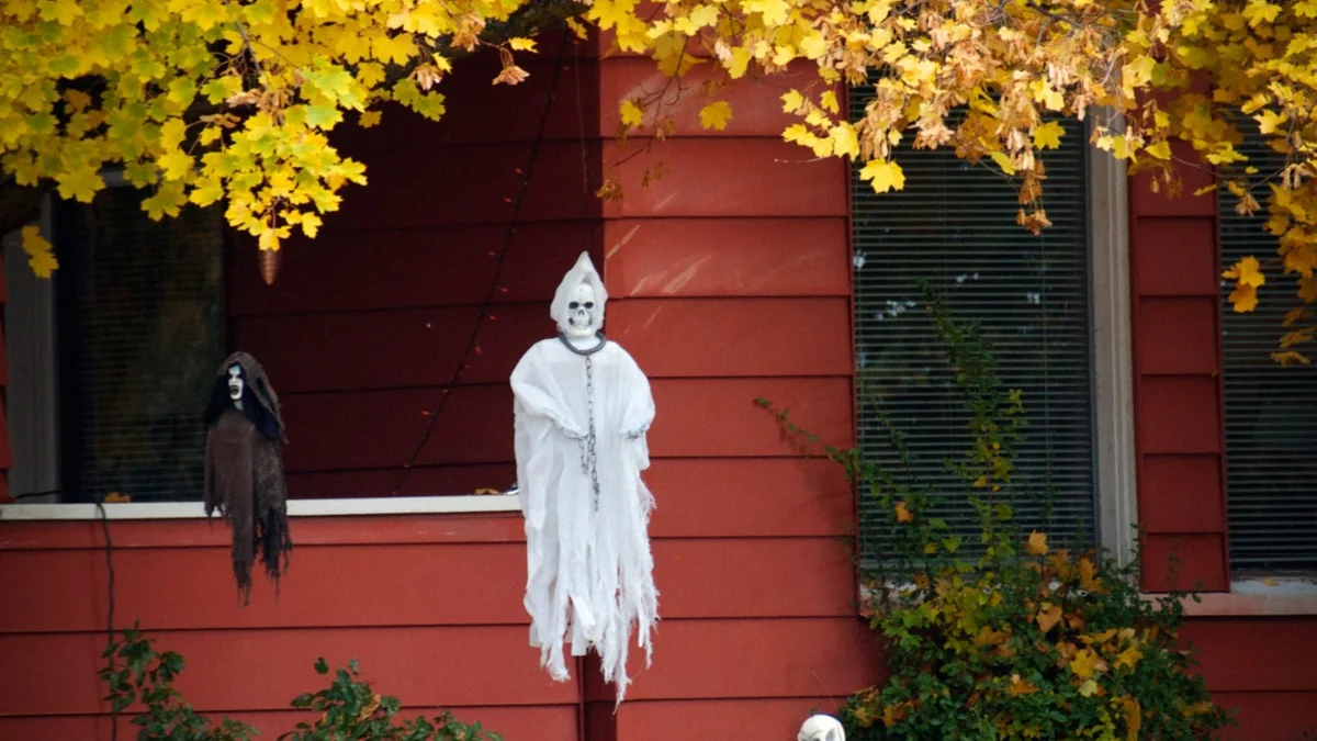 Outdoor autumnal front garden with weathered gravestones nestled among golden fall leaves and hanging draped ghouls