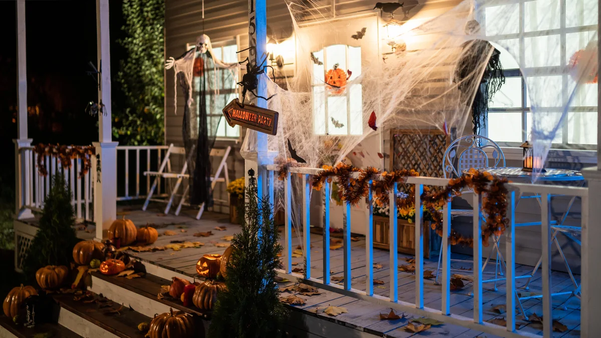 Atmospheric front porch featuring weathered wood Halloween party directional sign, carved lit pumpkins, and gossamer webs