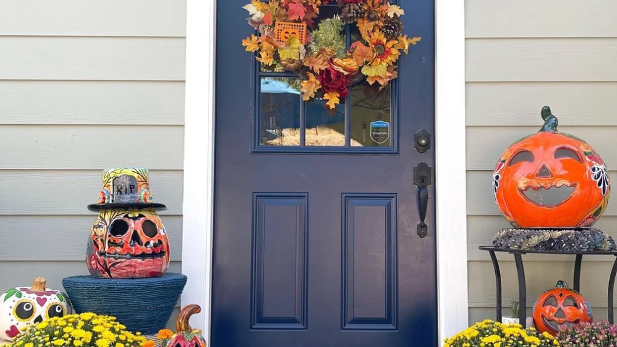 Cohesive porch styled in charcoal and burnt orange tones with artisan ceramic jack-o'-lanterns, floral wreath, and layered doormats