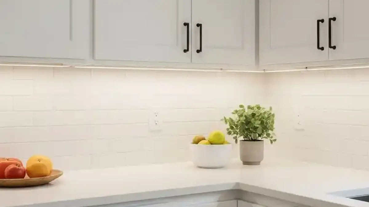 Continuous warm LED strip lighting running beneath kitchen upper cabinets illuminating a marble backsplash and countertop