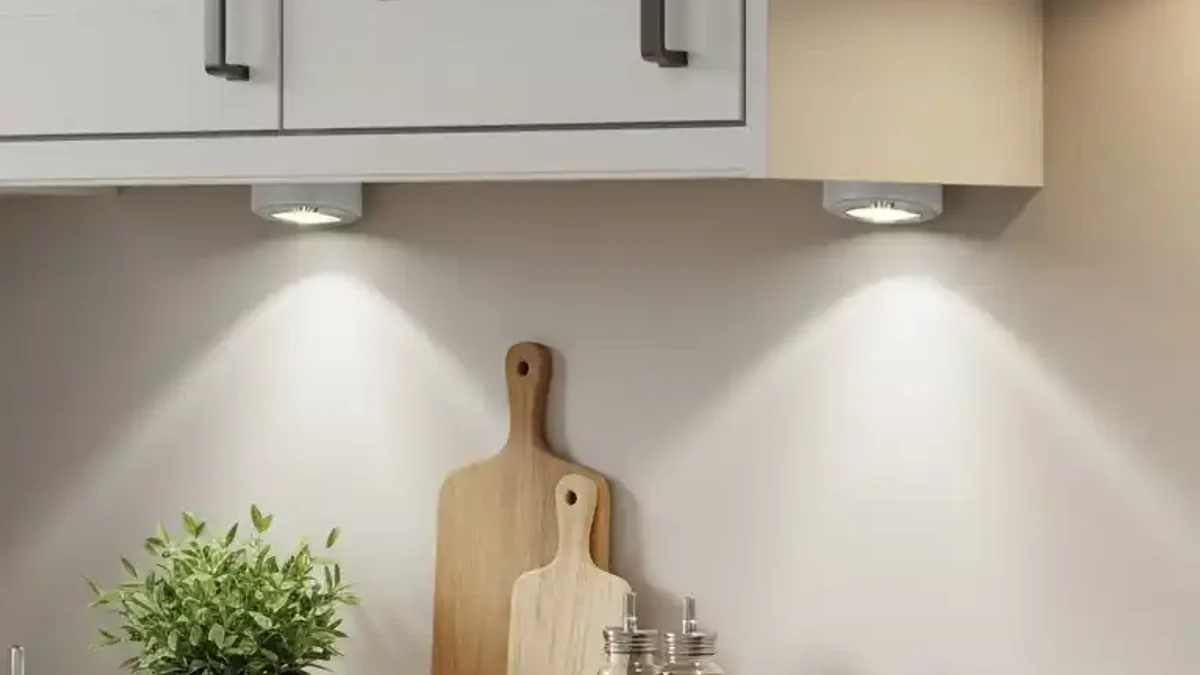 Round warm LED puck lights mounted under dark wood kitchen cabinets casting dramatic scalloped light cones across the backsplash